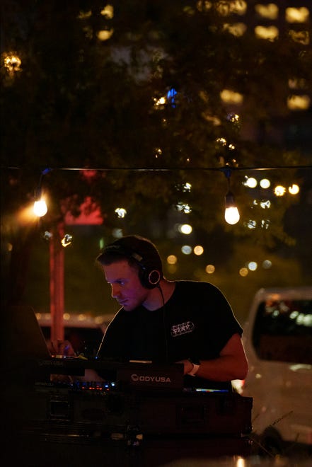 A DJ plays music for people as they fill the streets for the First Friday art walk on Roosevelt Row on Aug. 4, 2023, in downtown Phoenix.