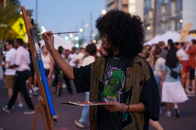 Shyla Ferrell paints as people fill the street for the First Friday art walk on Roosevelt Row on Aug. 4, 2023, in downtown Phoenix.